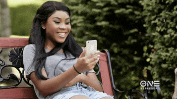 TV gif. Ajiona Alexus as DeAnna on The Rickey Smiley Show. She's sitting on a bench FaceTiming someone and she throws her head back and laughs heartily.