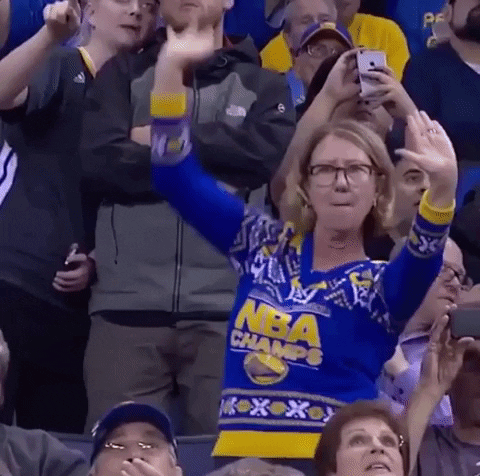 Sports gif. A female Golden State Warriors fan, wearing a Warriors-themed Christmas sweater in the crowd, raises the roof and whips out an imaginary lasso, dancing wildly. We can only assume she's on the jumbotron, right?