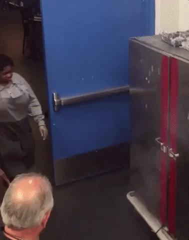 Video gif. Woman wearing an apron walks over to a metal cabinet and opens the door to reveal that everything inside the cabinet is on fire. As burning debris falls to the floor, she calmly assesses the situation, attempts to blow on the fire, then gives up, swinging the cabinet door shut with a “this is fine” attitude.