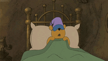 Movie gif. Winnie the Pooh from The Many Adventures of Winnie the Pooh. He has an eye mask and sleep hat on and is getting cozy in bed. He smiles and turns around, launching himself at his pillow as he cuddles with it.