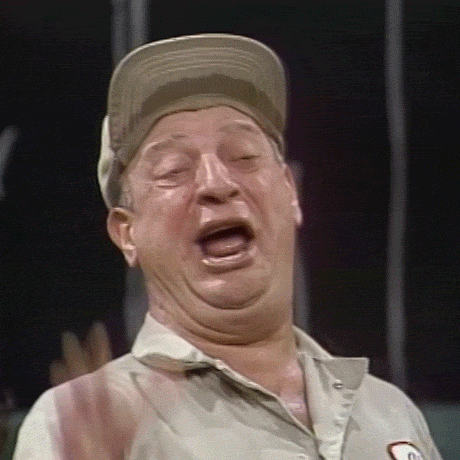 Celebrity gif. Rodney Dangerfield dressed as a car mechanic with his hand making an OK sign, bobbing back and forth while laughing.