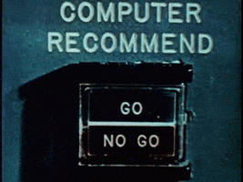Video gif. Archival footage of a mechanical box labeled, "Computer Recommend." A flashing blue rectangle on the box highlights the word, "Go."