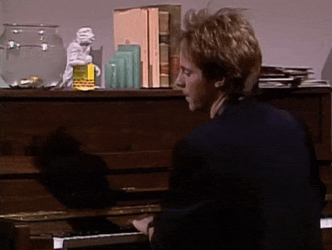 Gif of derek stevens playing piano, turning around to nod and smile.