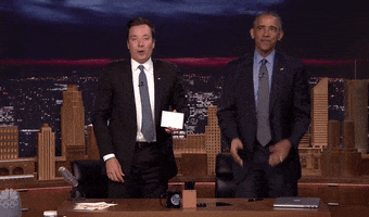 TV gif. Standing behind the desk of The Tonight Show next to Jimmy Fallon, Barack Obama claps and waves to us and says, “Thank you.”