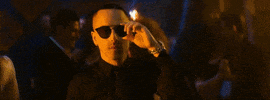 Music video gif. Yandel makes eye contact with a woman walking past the bar and he stares in awe, slowly taking his sunglasses off to get a better look at her.
