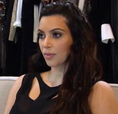 Reality TV gif. In a scene from Keeping Up with the Kardashians, Kim Kardashian slowly turns a blank look into a knowing smirk.