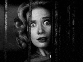 Movie gif. Mary Hilligoss as Mary Henry in Carnival of Souls looks through the bars of a metal gate. She breathes heavily and her eyes are wide with terror, with one eye bigger than the other.