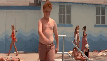 Movie gif. Patrick Renna as Hamilton "Ham" Porter in Sandlot confidently waves as he walks shirtless around the pool.