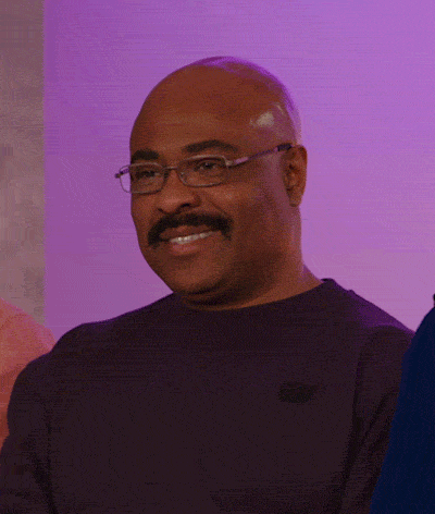 Video gif. Man with glasses and a mustache smiles and looks around awkwardly.