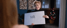 SNL gif. Smiling sarcastically, Kate McKinnon as Hillary Clinton holds cue cards and pulls them one by one, endlessly dropping them to the floor. Each cue card reads, “HA.”