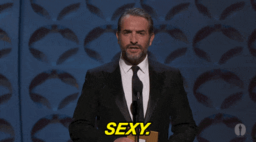Celebrity gif. Jean Dujardin is presenting an award at the Oscars and he stands in front of the podium and raises his eyebrows and smiles while saying, "Sexy."