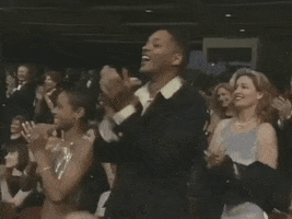 Celebrity gif. The audience at the 1997 Oscars all clap and stand up in a standing ovation. Will Smith looks up at the stage with a proud smile and claps.