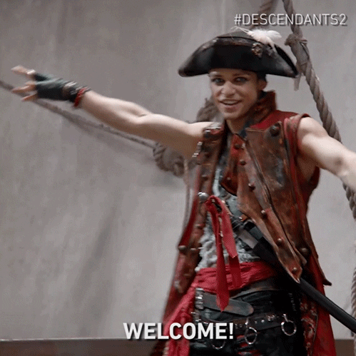 Disney gif. Thomas Doherty as Harry Hook in Descendants 2 dressed as a pirate on a ship, with his arms open wide, saying "welcome!"