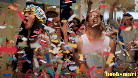 Movie gif. Eduardo Franco as Theo in Booksmart, wearing a shower bonnet, joins his classmates in celebrating in the hallway as confetti streams down from the ceiling.
