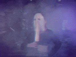 Video gif. A person wearing a crop top and a Michael Myers mask sexily body rolls and drags a prop knife down its body. 