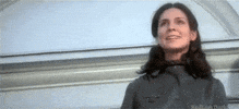 Movie gif. Holly Palance as a nanny in The Omen, standing on a ledge with a noose around her neck, looking honored.