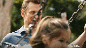 TV gif. Justin Harley as Kevin on This Is Us raises his arms in excitement as he watches a woman push a young girl on a swing.