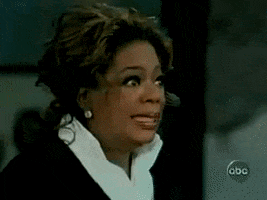 TV gif. Oprah Winfrey stares straight ahead with wide eyes and a forced smile through gritted teeth. Her eyes quickly flash to one side before looking back like she's extremely uncomfortable with what's happening. 