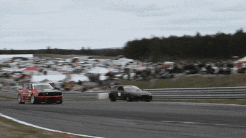 Sports gif. Black Toyota attempts to pass a red car on the side of a race track, then jumps back onto the track, losing its rear spoiler and crashing in the process.
