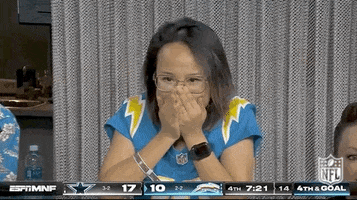 Video gif. Woman in a Los Angeles Chargers jersey is super pumped up as she watches the game with intensity, covering her mouth tightly then clenching her fists and shaking with adrenaline like her whole life depends on this moment.