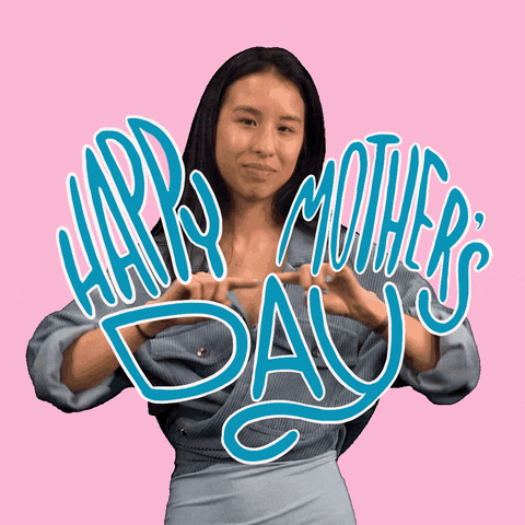 Digital art gif. Smiling woman draws the outline of a large cartoon purple heart with her hands in the air. In front of her, blue text reads, "Happy Mother's Day," everything against a baby pink background.