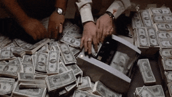 Video gif. Stacks of cash scatter the floor. One pair of hands shifts through the money while another pair of hands feeds dollars through a money counter.