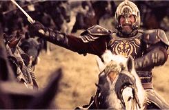 Movie gif. In a scene from The Lord of the Rings, The Return of the King, an angry, armored Bernard Hill as Theoden moves along the front lines of his battalion on horseback, striking the soldiers' swords with his.
