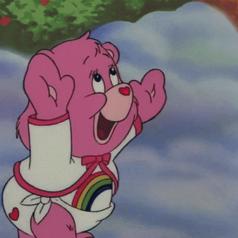 Cartoon gif. Cheer Bear from Care Bears reaches toward the air with a wide-eyed joyous expression and catches a red heart-shaped bubble that pops in its hands while another bubble floats by.