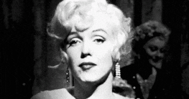 Celebrity gif. Marilyn Monroe is shot in black and white and she pouts at the camera while rolling her eyes and shrugging her shoulders.
