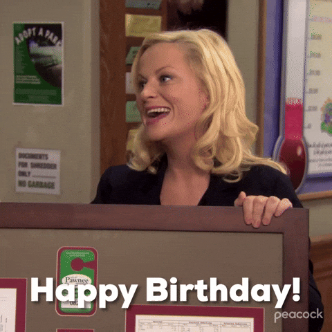 Parks and Recreation. Amy Poehler as Leslie leans on a cubicle wall and smiles genuinely as she says "Happy birthday," which also appears as text.