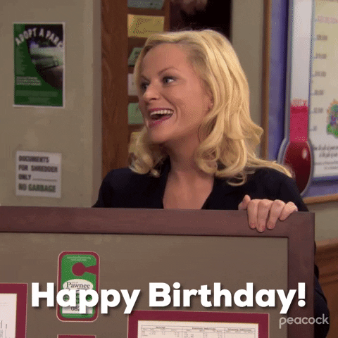 Parks and Recreation. Amy Poehler as Leslie leans on a cubicle wall and smiles genuinely as she says "Happy birthday," which also appears as text.