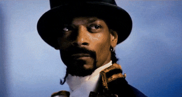 Celebrity gif. A dramatically lit Snoop Dogg wearing a top hat nods his head with resolve.