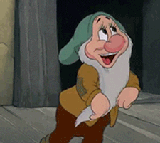 Disney gif. Bashful, a long, gray bearded dwarf with a green cap looks up with large eyes. His pale turns bright red as he lowers his gaze and turns his head, placing a finger to his mouth and making a shy innocent grin.
