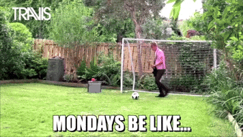 Video gif. A man playing the guitar kicks a soccer ball, which flies through the air and hits another man, also singing and playing guitar, in the face. Text, "Mondays be like"