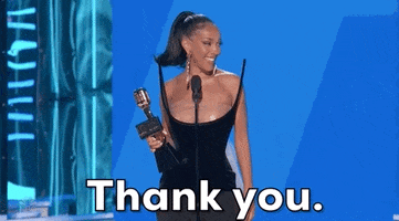 Celebrity gif. Doja Cat stands on stage at the Billboard Music Awards holding a trophy and smiling as she blows a kiss. 