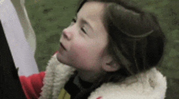Video gif. A young girl turns to the camera and smirks knowingly.