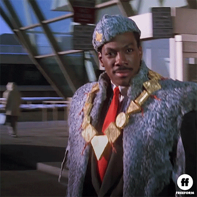 Movie gif. Eddie Murphy as Akeem in Coming to America wearing elaborate royal attire and a giant gold necklace walks out of an airport and holds up a hand. Caption reads, "Halt."