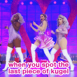 TV gif. Three queens performing a dance number on RuPaul's Drag Race, one pushing the other two out of the way. Hot pink text, "When you spot the last piece of kugel."