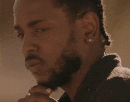 Celebrity gif. Kendrick Lamar looks over his shoulder, pensively stroking his goatee.