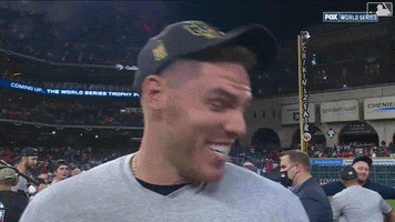 Sports gif. Freddie Freeman cracks up as he turns his head to the side, then rubs his eye as he stands on a baseball field.