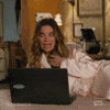 Schitt's Creek gif. Annie Murphy as Alexis lounges in a robe on a bed in front of an open laptop. She looks at the laptop, her eyes widening comically, twists her hair in her hand and says what appears as text, "Yum!"