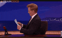 Celebrity gif. Talk show host Conan O'Brien looks up from a sheet of paper and pretends like he's shocked to see us. He turns to face us and sets the paper down, saying, "Oh, hello there!"