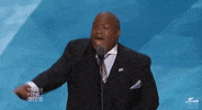 Political gif. Mark Burns is speaking at a podium and he raises his hand in the air while giving a rallying fist pump.