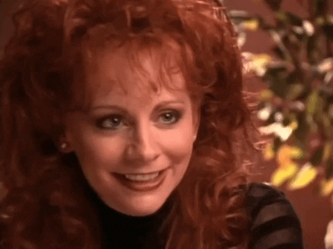 Music video gif. Reba in her music video for "Why Haven't I Heard From You." She smiles and raises her eyes expectantly. 