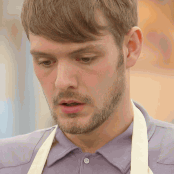 Reality TV gif. John Whaite from the Great British Bake Off exhales, blowing out his cheeks, appearing frustrated.