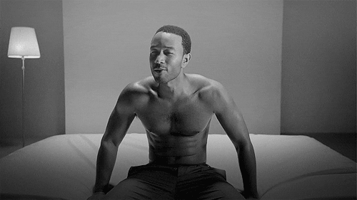 Celebrity gif. John Legend sits on a mattress, wearing a pair of pants. He holds his arms out, gripping the side of the bed to perfectly display his muscles. He gazes at us as he sings. 