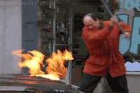 Seinfeld gif. Jason Alexander as George frantically whacks the hood of a car on fire with a corn broom that also catches fire.