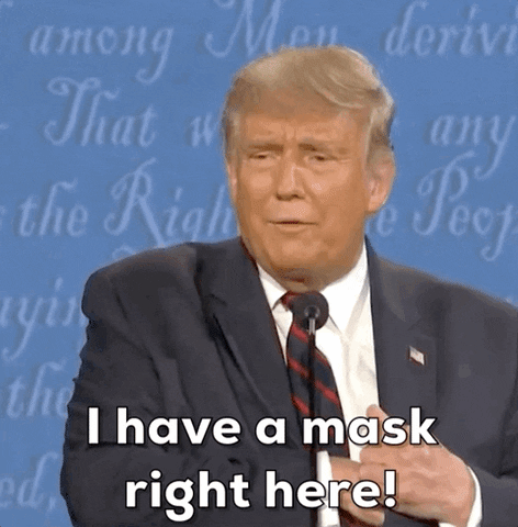 Political gif. Donald Trump stands behind a microphone at a presidential debate. He has a smug look on his face as he whips a face mask out of his suit jacket. He says, “I have a mask right here!”