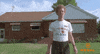 Movie gif. Standing in front of his home, Jon Heder as Napoleon Dynamite awkwardly waves and says "hi." 