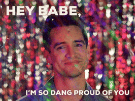 Celebrity gif. Brendon Urie of Panic! At the Disco smiles and shakes his head, raising his eyebrows as confetti falls around him. Text, “Hey babe, I’m so dang proud of you.”